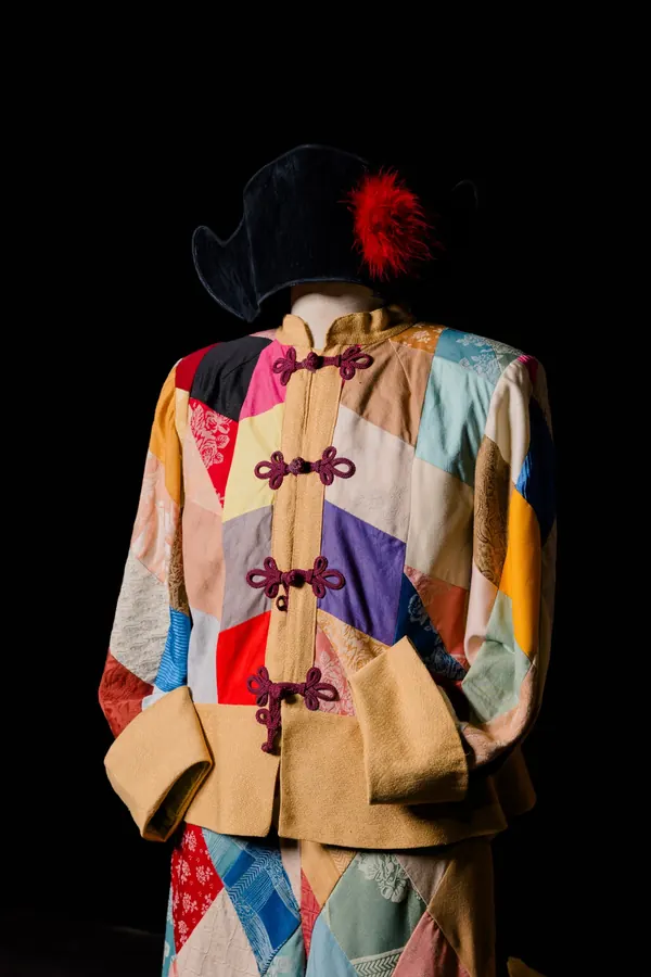 Costume di Arlecchino in patchwork di tessuti colorati con alamari, e cappello nero con piuma rossa