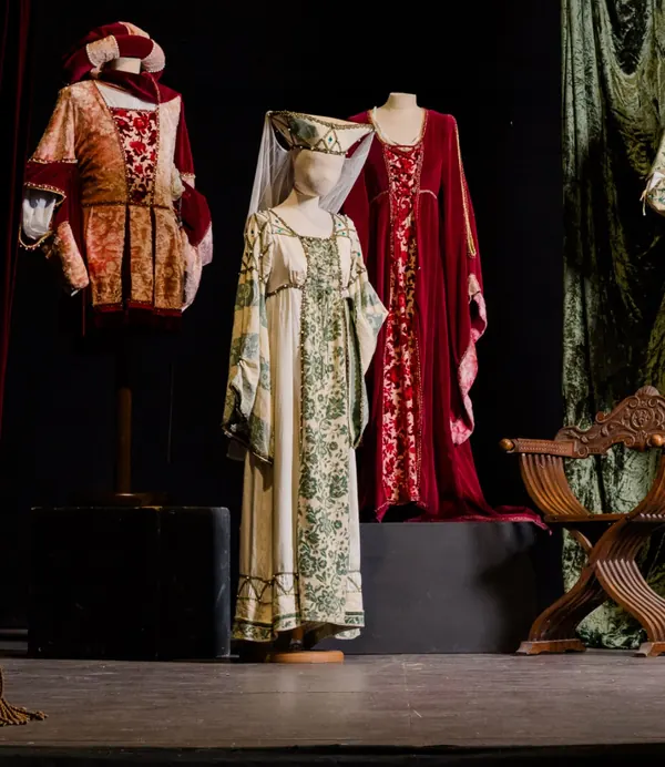 Costumi medievali in velluto rosso e broccato verde, con un copricapo a cono e velo