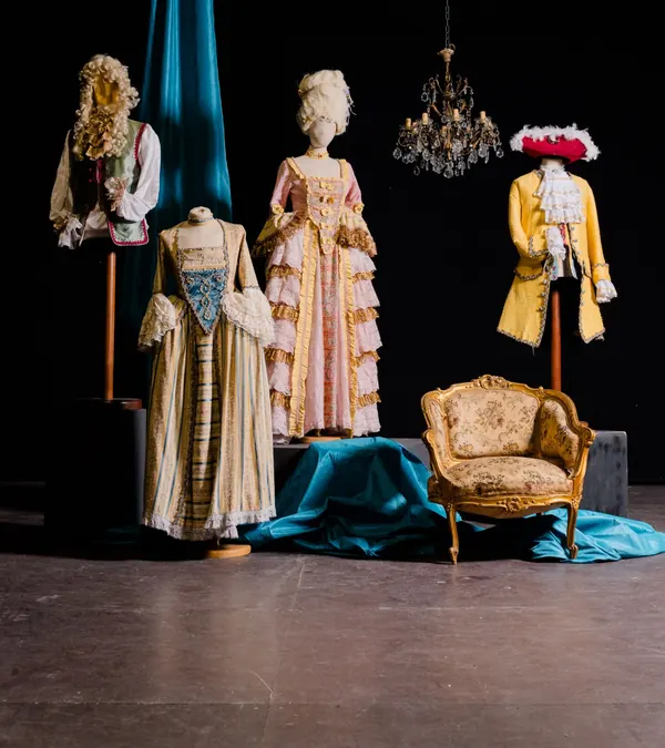 Costumi del Settecento: abito rosa a balze, abito a righe con pettorina azzurra, giacca gialla e poltroncina dorata