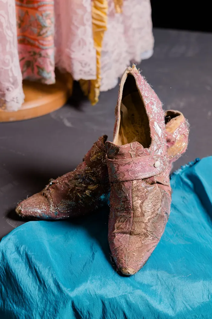 Scarpe d'epoca in broccato rosa e argento, appoggiate su seta color petrolio