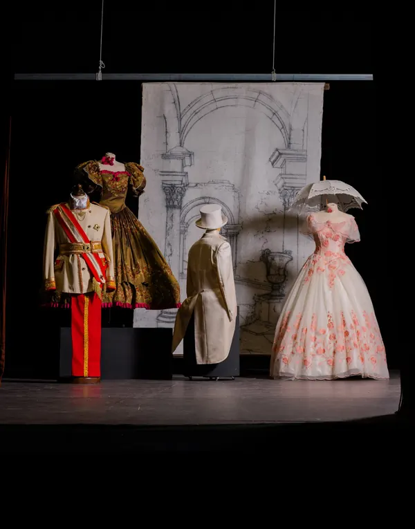 Fondale con archi e colonne disegnati, appeso sul palcoscenico dietro costumi dell'Ottocento