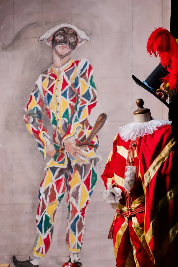 Fondale dipinto con la figura di Arlecchino, davanti a un costume rosso e oro su manichino