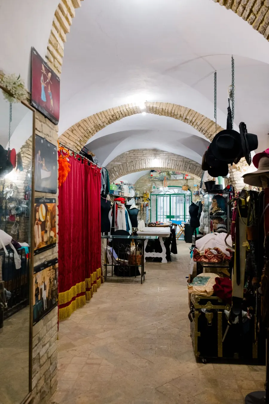 L'interno della bottega nel centro storico di Vasto: volte in mattoni, un camerino con sipario rosso e frange dorate, cappelli appesi, bauli e manichini